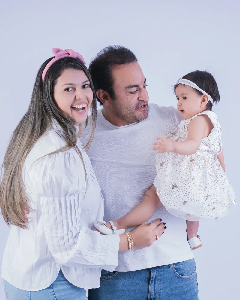 Mãe, pai e filha bebê no colo rindo juntos em ensaio de família no estúdio