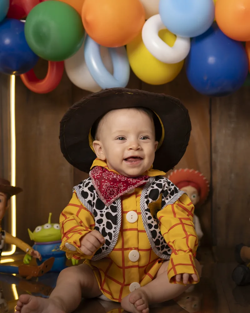Bebê de 1 ano fantasiado de cowboy em ensaio Smash the Cake com cenário temático de balões
