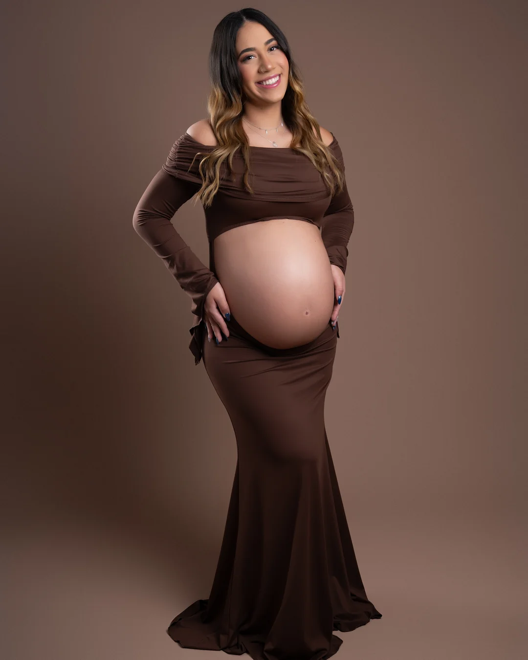 Gestante sorrindo com as mãos na barriga, vestido marrom