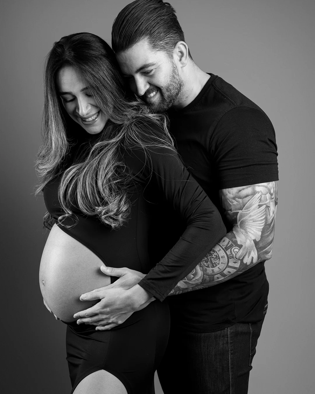 Casal em preto e branco, mãos na barriga da gestante