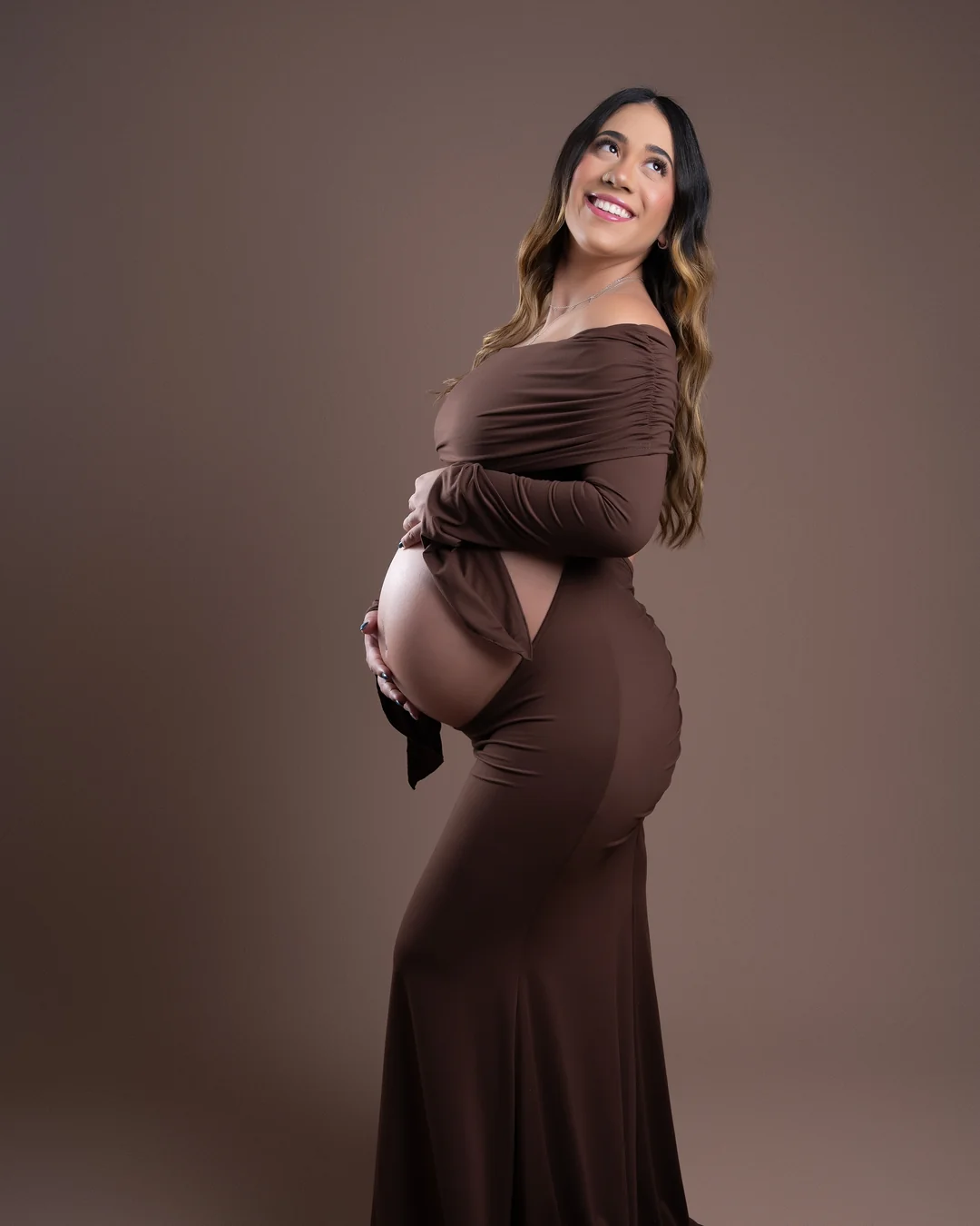 Gestante sorrindo de perfil, vestido marrom longo