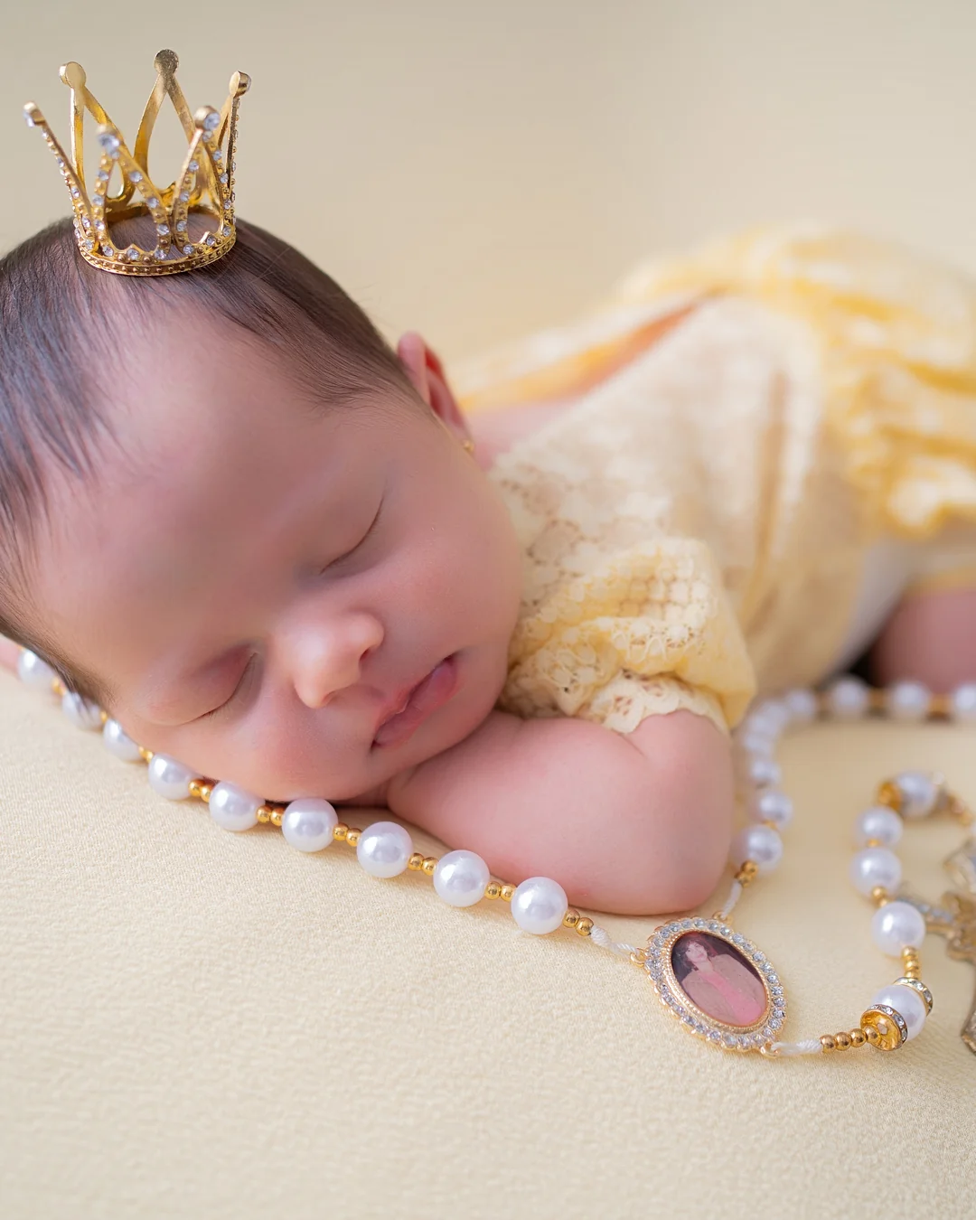 Recém-nascida com coroa e terço de pérolas, vestido amarelo