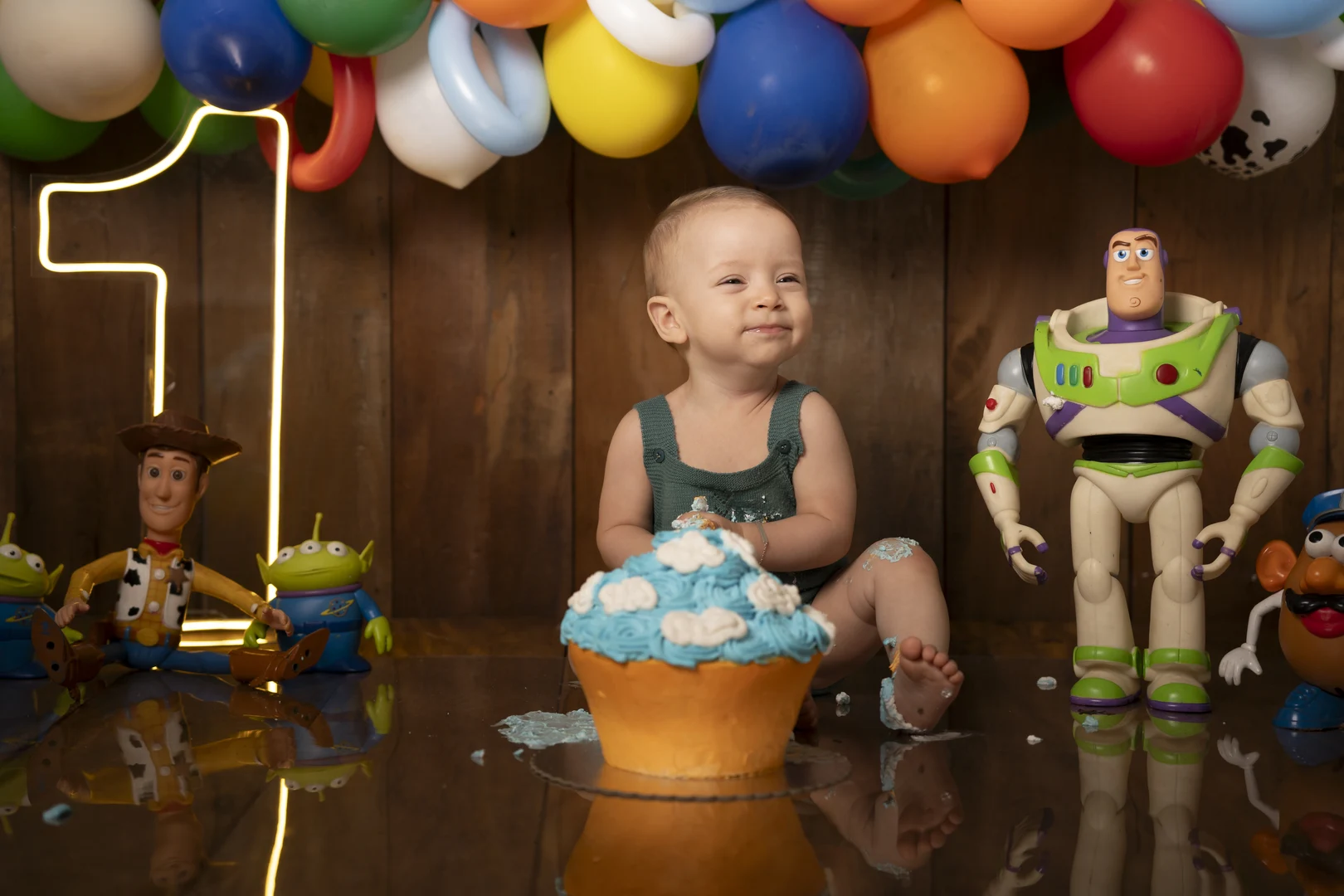 Bebê sorrindo ao lado do bolo, tema Toy Story